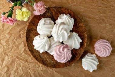 Beyaz ve pembe kurabiyelerin üst görüntüsü. Geleneksel çırpma merengi, fırınlama kremi ya da çiçek eşliğinde el işi kâğıdı zemininde zıpla.