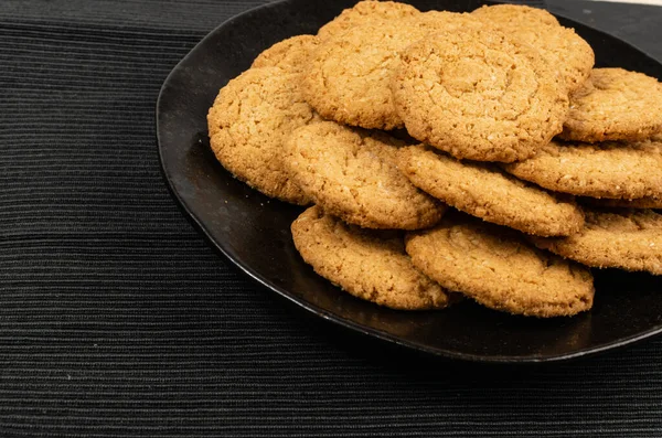 Thin oatmeal cookies, cereal oat crackers on black background. Crispy anzac biscuit cookie with oat flakes closeup