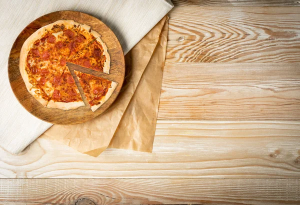 Pepperoni pizza on wooden plate top view with copy space. Rustical kitchen mock up with traditional Italian pizza on craft paper