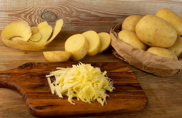 Ahşap kesim tahtasında çiğ patates. İsviçre patatesi için ızgara ve dilimlenmiş patates yığını ya da klasik doğrama tahtasında krep.