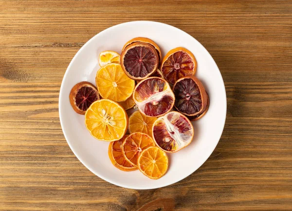 Dried slices of orange and blood orange isolated on white background. Dry lemon, tangerine and sicilian orange on dark plate