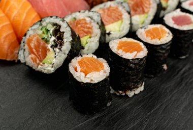 Dark Sate Plate Closeup 'ta çeşitli Japon suşi yemekleri. Nigiri ve Nori Maki Suşi Rolls with Raw Somon, Maguro Tuna, Unagi Yılanbalığı, Avocado, Salatalık, Yeşil Salata ve Philadelphia Peyniri