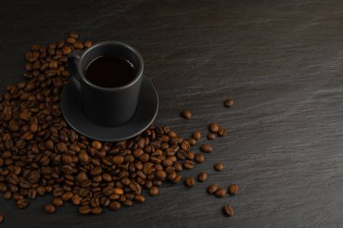 Üst manzara espresso fincanı ve siyah taş zemin üzerinde kahve çekirdekleri fotokopi alanı ile. Beyaz kahve ya da bardakta sıcak içecek.