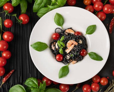 Siyah arka planda ev yapımı spagetti. Deniz mahsullü erişte, karidesli makarna. Beyaz tabakta siyah İtalyan spagtosu.