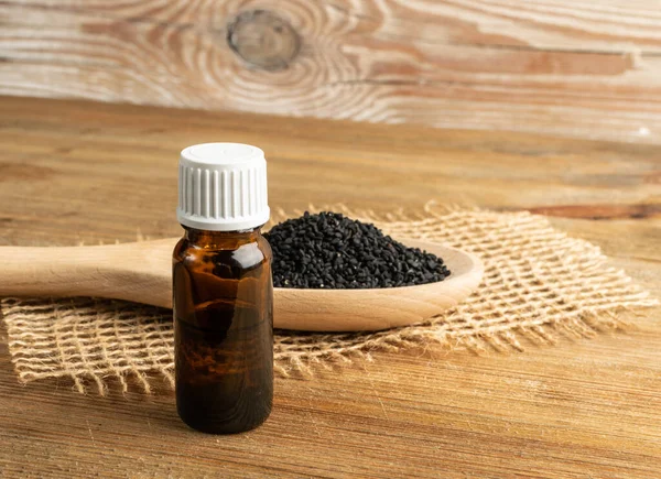 Black cumin oil in small vintage bottle on wood table. Caraway seeds organic essential oil, tincture, extract, infusion. Nigella sativa tincture, essence