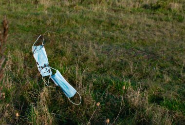 Maske kirliliği konsepti. Park çimenleri üzerinde tek kullanımlık tıbbi maskeler. Tek kullanımlık tıbbi maske atığı, çevre hasarı