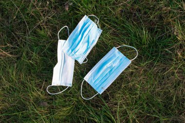 Maske kirliliği konsepti. Park çimenleri üzerinde tek kullanımlık tıbbi maskeler. Tek kullanımlık tıbbi maske atığı, çevre hasarı