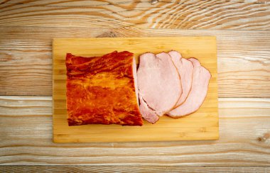 Tütsülenmiş domuz filetosu, dilimlenmiş jambon, ahşap masa arkasındaki et filetosu.