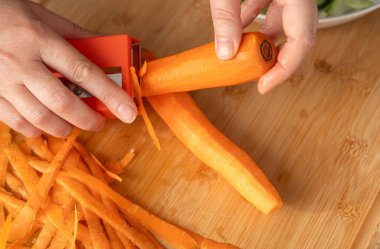 Bıçakla taze havuç soyma yakın plan, çiğ havuç dilimleri, portakal kökü sebzesi, havuç kesme tahta arka plan, seçici odak