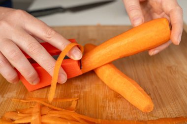 Bıçakla taze havuç soyma yakın plan, çiğ havuç dilimleri, portakal kökü sebzesi, havuç kesme tahta arka plan, seçici odak