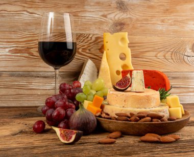 Peynir tabağı çeşitliliği, sarı, beyaz ve mavi gorgonzola tabağı kırmızı şarap bardağı, peynir tahtası, çeşitli doğranmış süt ürünleri, ahşap üzerinde kokulu Fransız peyniri.