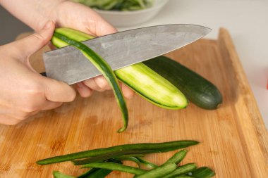 Ahşap yemek tahtasında büyük bir bıçakla salatalık soyuyordum. Taze sebze salatası yapan bir kadın evde yemek pişirir.