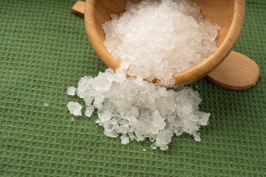 Ölü deniz tuzu yığını, vücut spa 'sı için beyaz kristaller, ezilmiş buza benzer sodyum klorür, ahşap kasedeki spa fırçası.