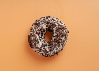 Çikolatalı çörekler izole edilmiş, kahverengi çörekler çok renkli serpiştirilmiş, donutlar turuncu arka planda.