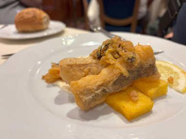Restoran tabağında lezzetli balık var. Kızarmış morina filetosu ile İngiliz yemeği. Polenta çubukları yakın plan, bulanık arkaplan.