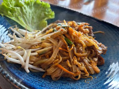 Pad Thai veya Phad tha Asya eriştesi yakından. Çin pirinçli makarna, etli Tayland yemeği, erişte, taze lahana salatası ve bulanık arka planda sokak restoranında yeşillikler.