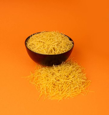 Turuncu arka planda çiğ vermicelli, yuvarlak altın çorba makarna, dağınık ev yapımı erişte, ince makarna, siyah kâsenin yanında İtalyan usulü makarna.