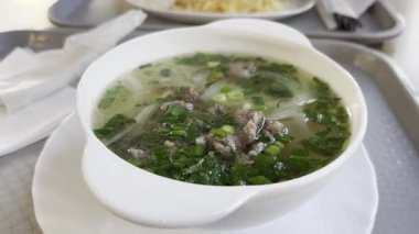 Vietnam şeffaf çorbası, pirinç eriştesi, et ve beyaz kasede yeşillikler. Sıcak şeffaf çorba, pirinç makarnası ve çeşitli katkı maddeleri.