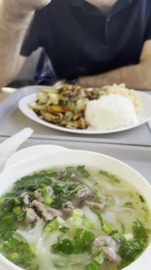 Vietnam şeffaf çorbası, pirinç eriştesi, et ve beyaz kasede yeşillikler. Sıcak şeffaf çorba, pirinç makarnası ve çeşitli katkı maddeleri.