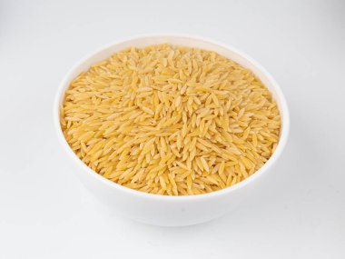 Kavanozda çiğ orzo makarna yığını. Büyük pirinç tanesine benzeyen risoni makarnası, beyaz arka planda Yunan Kritharaki yığını.