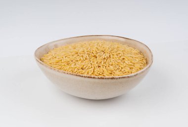 Kavanozda çiğ orzo makarna yığını. Büyük pirinç tanesine benzeyen risoni makarnası, beyaz arka planda Yunan Kritharaki yığını.