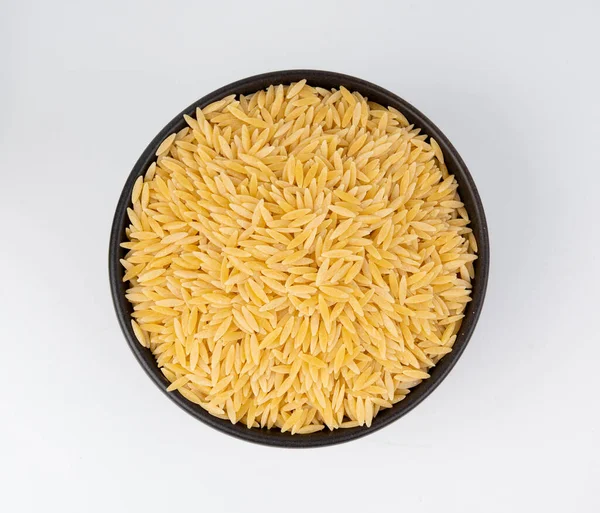 Kavanozda çiğ orzo makarna yığını. Pirinç tanesi şeklinde risoni makarnası. Beyaz arka plan manzaralı Yunan Kritharaki yığını.