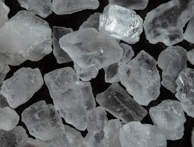 Koyu arkaplanda büyük tuz kristallerinin makro çekimi. Şeffaf yüzeylerin detaylı dokusu ve ışık oyunu. Mutfak içeriği, ambalaj tasarımı veya soyut arkaplan için mükemmel.
