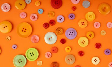Renkli dikiş düğmeleri deseni. Turuncu arkaplan görünümünde kumaş, terzi aksesuarı koleksiyonu için farklı renk ve boyutlarda plastik dikiş düğmeleri
