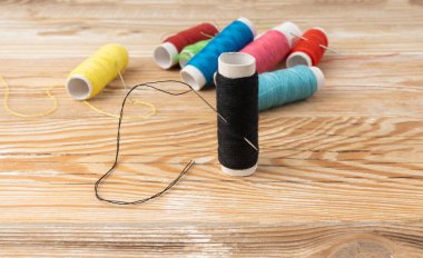 İğne ve yeşil, sarı, kırmızı iplik. Tahta arka planda iğne, dikiş malzemesi, pamuk ipliği boyası, kumaş ve terzilik sektörü sembolü