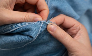 Kadın kot kumaşında iğne ve yamayla kotları elleriyle onarıyor. Giysi onarımı sanatsal dikiş ve tekstil geri dönüşümünü ön plana çıkarıyor