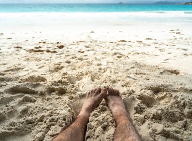 Tropikal sahildeki sıcak kumda dinlenen çıplak ayaklar yaz rahatlama, özgürlük, tatil havası, açık hava keyfi, güneşli kaçış sırasında doğal basitlik ve refahı simgeliyor.