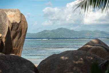 Anse Source d Argent sahilinin tropikal köşesinde granit kayalar yeşil yapraklar ve okyanus manzarasıyla Seyşeller Adası 'ndaki uzak bir adaya doğru.