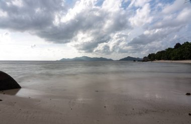 Anse Source d Argent plajı yumuşak kumlu sakin deniz ve dramatik bulutlar La Digue Adası Seyşelleri 'ndeki uzak adalara bakıyor
