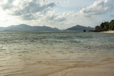 Anse Source d Argent sahilinde akşam ışığı granit kayalar berrak su ve Seyşeller Adası 'ndaki uzak adaların manzarası