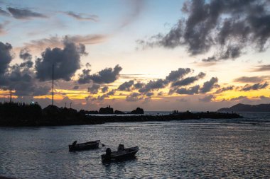 Alacakaranlıkta La Digue marinası. Suyun üzerindeki küçük tekneleri ve renkli gökyüzü altındaki Praslin adasının uzak manzarası.