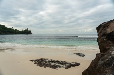 Bulutlu bir günde, soluk renkleri, soluk okyanusu ve bulutlu gökyüzü olan beyaz Seyşeller plajı.