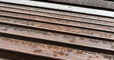 Su püskürtücü kaplama üzerine yağan yağmurdan sonra Modern Benç. Açık Şehir Mimarisinin Tahta Yüzeyine Büyük Damlalar. Islak Açık Sandalye, Şehir Mobilyaları, Boş Plank Koltuk Deseni