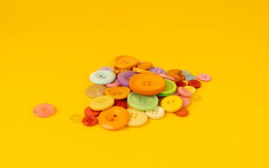 Çok renkli dikiş düğmeleri yığını. Sarı arkaplan görünümünde kumaş, terzi aksesuarı koleksiyonu için farklı renk ve boyutlarda plastik dikiş düğmeleri