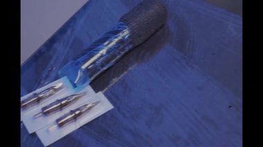 Steril iğneler, mürekkep bardakları ve petrol jölesiyle dövmecilerin çalışma yerinin yakın çekimi.