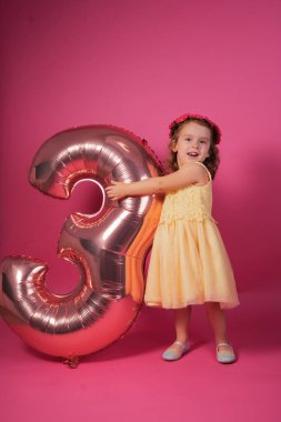 Mutlu çocuk doğum gününü kutluyor, pembe arka planda üç numaralı balonla duruyor.