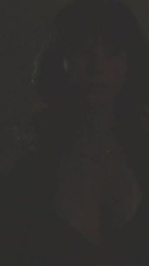 Siyah ceket ve sutyen giyen seksi esmer model dramatik stüdyo ışıkları altında poz veriyor.