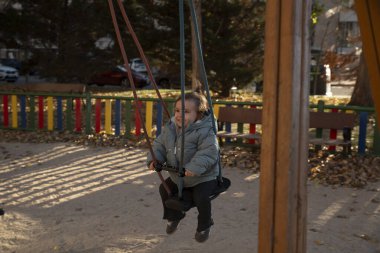 Güneşli bir günde parkta salıncakta gülümseyen ve oynayan küçük bir çocuk.