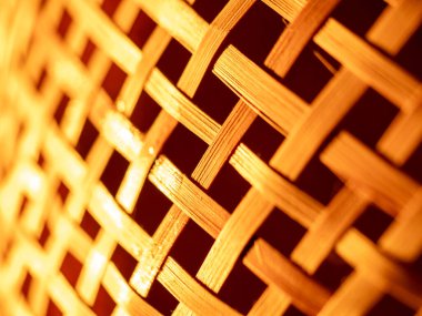 Hasır sepetin yakın çekim makrosu karmaşık bir bambu dokuma deseni ve sıcak kehribar aydınlatma, doğal dokuyu, işçiliği ve arka plan veya dekoratif kullanım için tekrarlanan geometrik çizgileri gösterir.