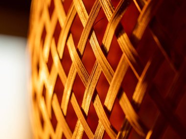 Hasır sepetin yakın çekim makrosu karmaşık bir bambu dokuma deseni ve sıcak kehribar aydınlatma, doğal dokuyu, işçiliği ve arka plan veya dekoratif kullanım için tekrarlanan geometrik çizgileri gösterir.