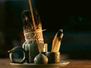 Ahşap tütsü çubuklarından hafif duman yükselir. Toprak tutucular sıcak bir seramik tabakta dinleniyor. Soluk ışık mum ışığı ya da gün doğumunu işaret ediyor. Dinginlik, sakinliği, meditasyonu veya ayini çağrıştırır.