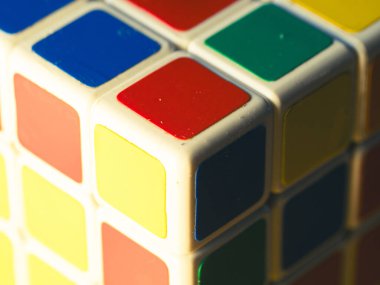 Renkli bir Rubik küp köşesinin makro fotoğrafı. Kenarları aşınmış sarı, kırmızı ve mavi çıkartmaları gösteriyor. Plastik desenli..