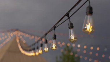 Yumuşak, bulanık bir arka plan ve sıcaklığı davet eden büyüleyici bokeh efektleriyle güçlendirilmiş, karanlık gökyüzüne karşı güzel bir şekilde asılı parlayan sicim ışıklarının büyüleyici atmosferini deneyimleyin..