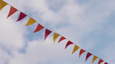 Yumuşak beyaz bulutlarla bezenmiş çarpıcı mavi gökyüzüne karşı dalgalanan renkli üçgen bayrakları deneyin, gerçek bir neşe ve şenlik sembolü..