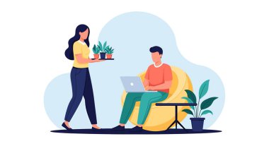 Bir kadın, sarı puf minderde oturan bir adama saksıda saksı bitkisi olan küçük bir masanın yanındaki dizüstü bilgisayarda çalışan bir tepsi saksı taşıyor..