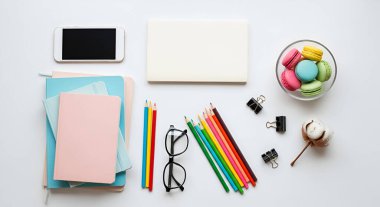 Dizüstü bilgisayarı, telefonu, defterleri, renkli kalemleri, gözlükleri, ataçları, dekoratif pamuk yumağı ve bir kase makaronu içeren temiz ve düzenli bir çalışma alanının genel görüntüsü..